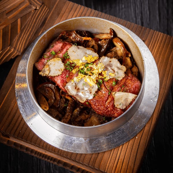 Wagyu beef with gold flakes and truffle slices, served in a metal pot on a wooden tray.