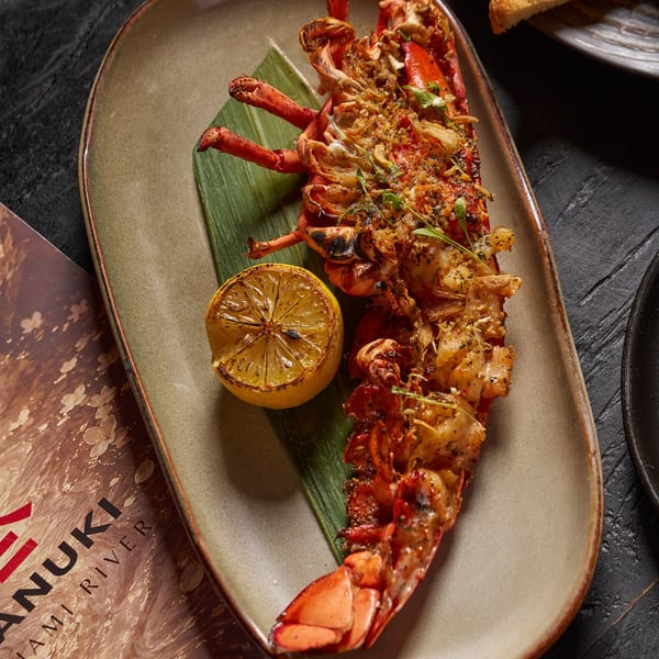 Grilled lobster topped with herbs and crispy garnish, served on a banana leaf with charred lime.