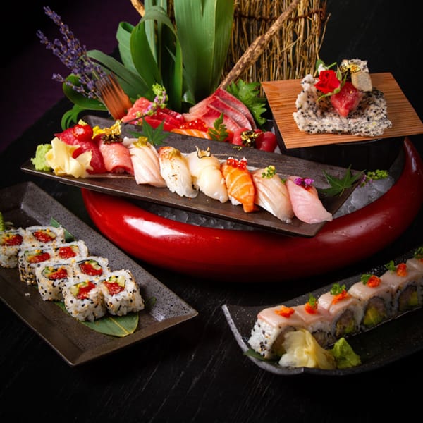 An array of colorful sushi, sashimi, and rolls artfully arranged on dark plates and a red boat.
