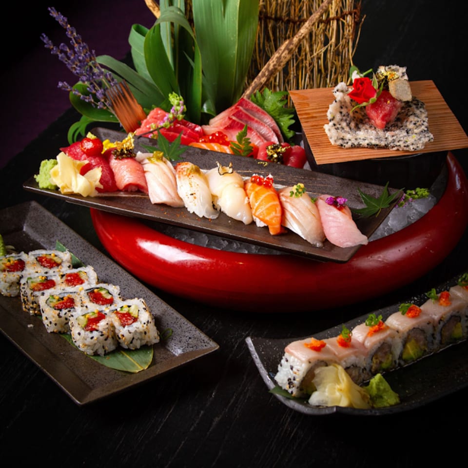 An array of colorful sushi, sashimi, and rolls artfully arranged on dark plates and a red boat.