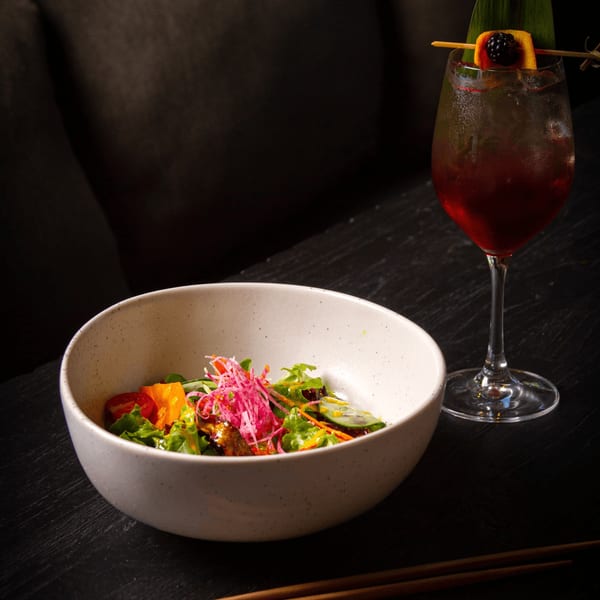 Asian-fusion salad with red cabbage and a dark cocktail garnished with a blackberry.