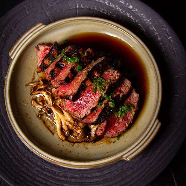 Grilled steak slices with mushrooms and green onions in a savory sauce on a ceramic plate.