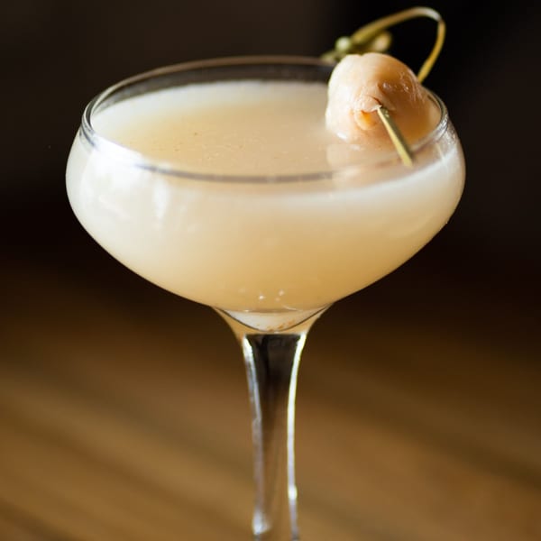 A Tanuki River Landing lychee martini, garnished with a lychee fruit on a skewer.