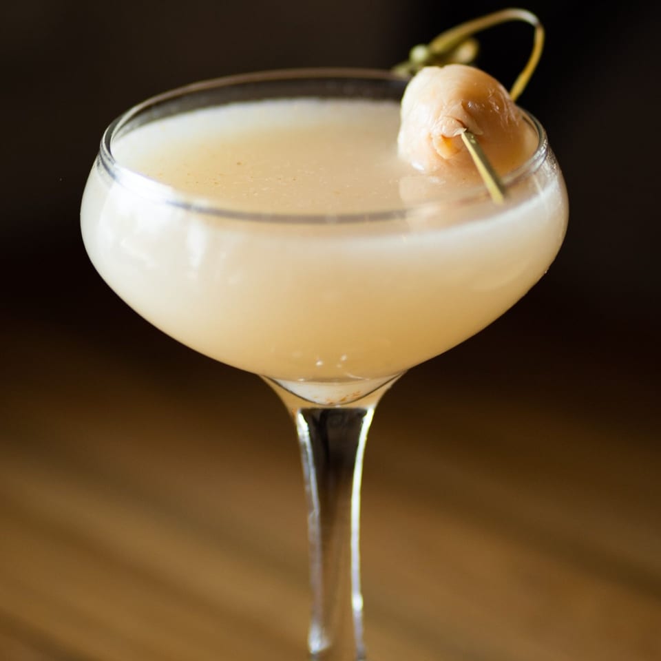 A Tanuki River Landing lychee martini, garnished with a lychee fruit on a skewer.