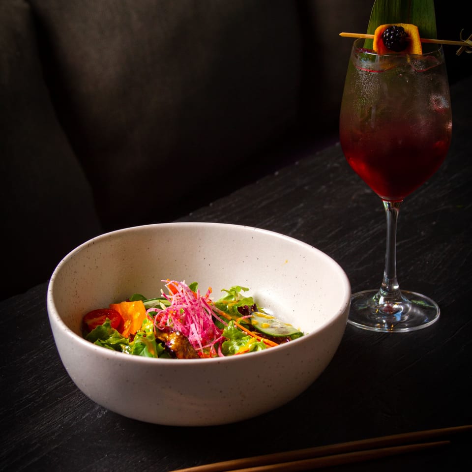 A colorful salad with red onions and a dark red cocktail with a blackberry garnish.