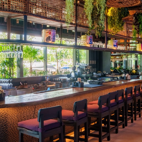 Tanuki River Landing's bar with wooden counter, purple stools, and lush greenery hanging overhead.