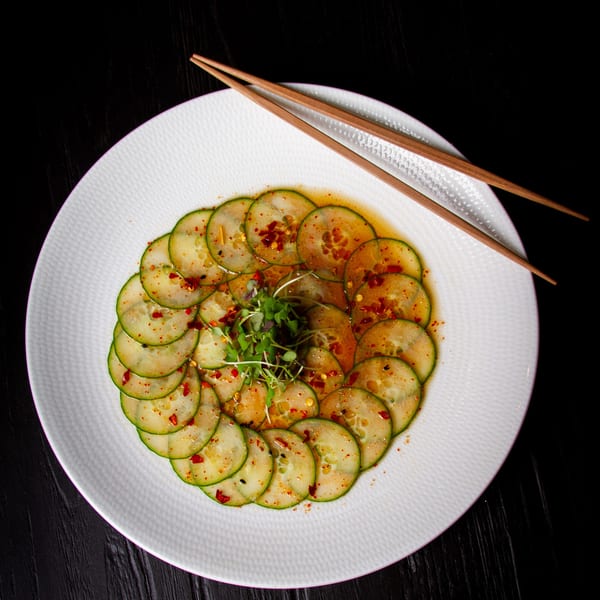Thinly sliced cucumbers arranged in a circle, drizzled with chili oil and topped with microgreens.